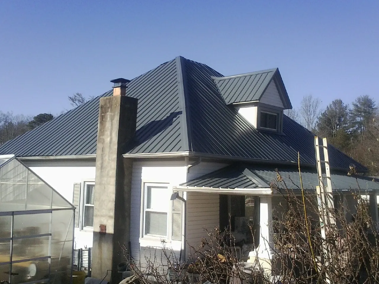 Dark blue standing seam metal roof on a white farmhouse with dormer — Slate & Tile Roof Repair by Roofing Brothers in Norborne