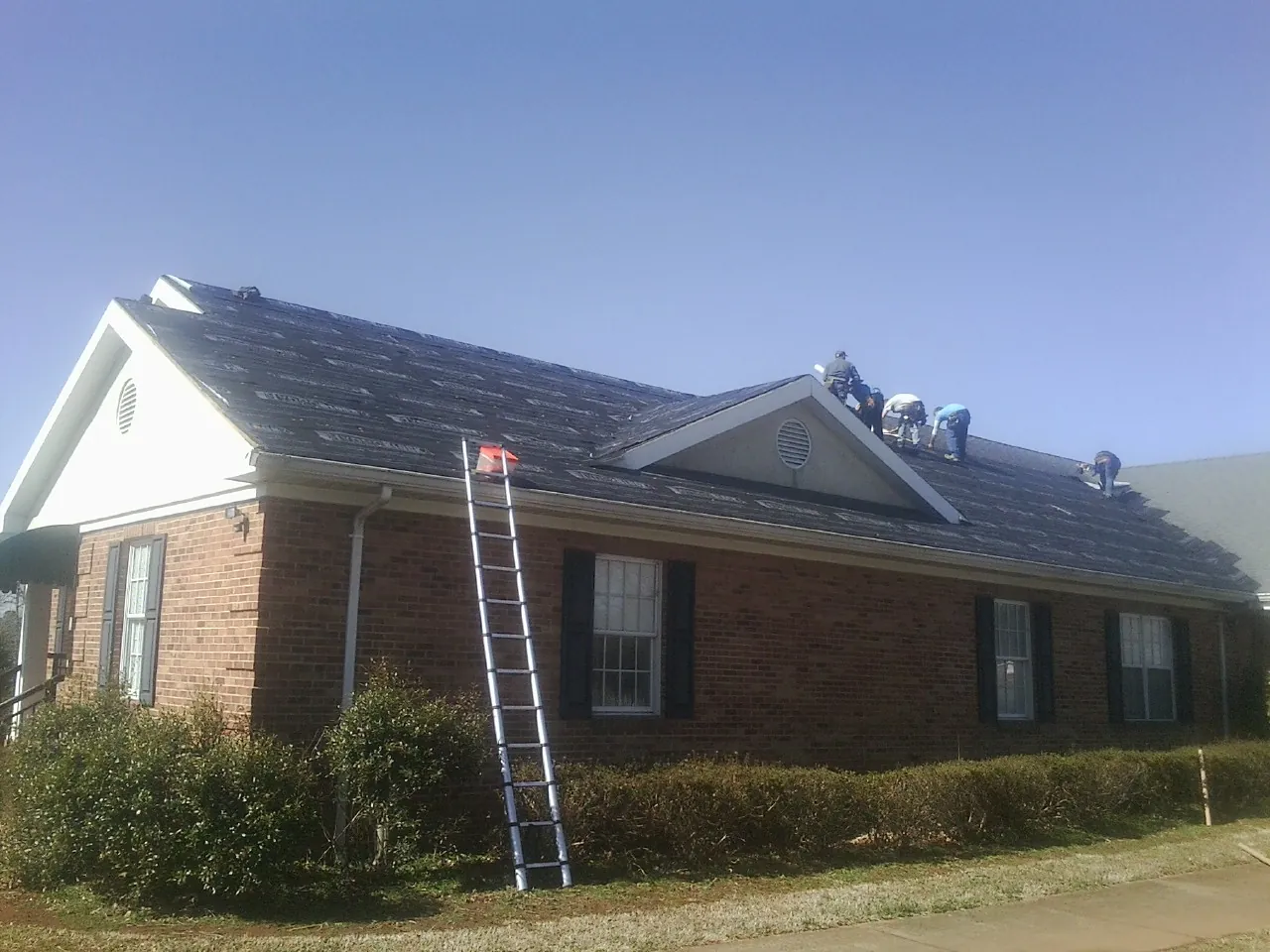 Crew tearing shingles off a brick ranch roof with a ladder set — Emergency Roof Repair work by our crew in Norborne