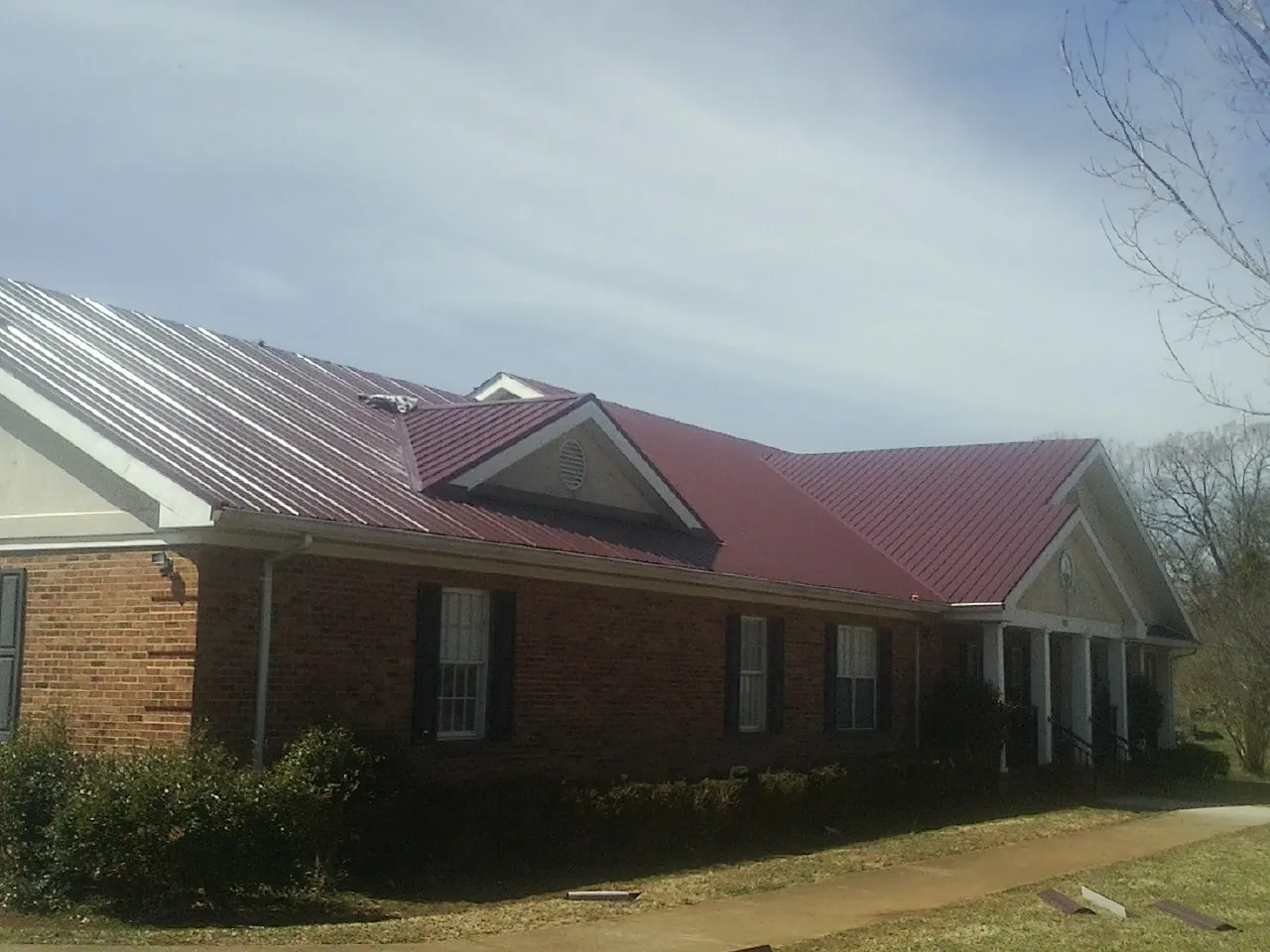 Red metal roof with gabled entries on a long brick building, from a Hail Damage Roof Repair job in Norborne