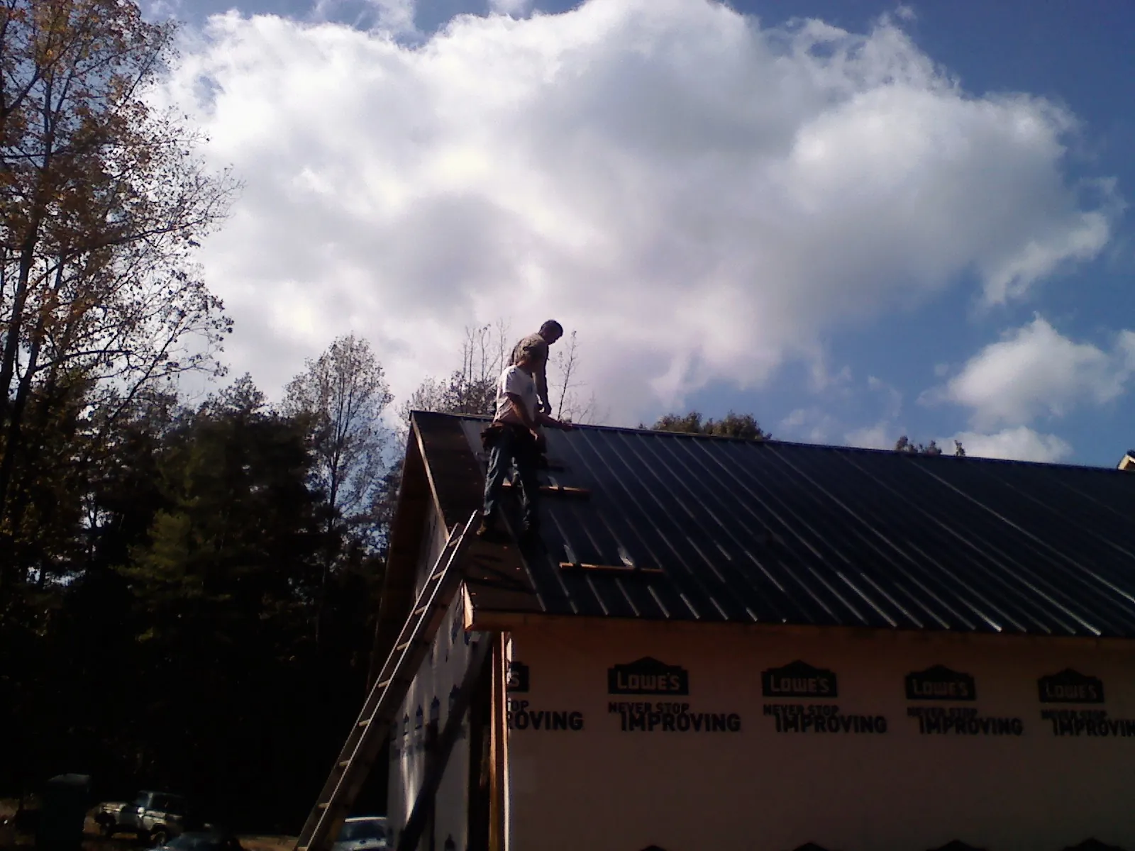 Roofer fastening dark metal panels high against a cloudy sky, from a Roof Inspection job in Norborne